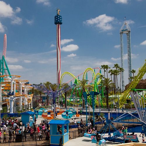 The image shows a vibrant amusement park with various colorful rides, roller coasters, and attractions filled with people enjoying their day.